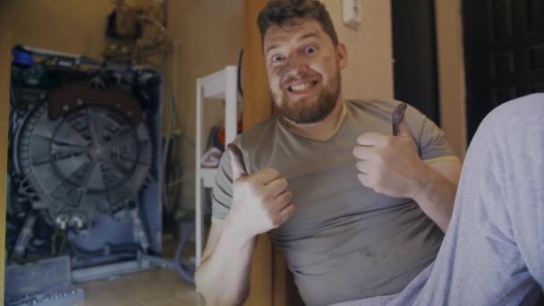 Чоловік радіє, що відремонтував пральну машину, показує пальці вгору — стокове відео