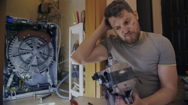 Orta yaşlı bir adam çamaşır makinesini kendi başına tamir etmekten yoruldu. — Stok video