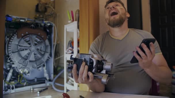 A man fixes a washing machine and watches instructions on his phone — Stock Video