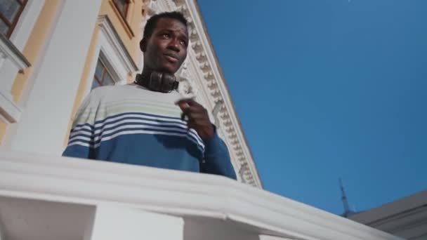 Um jovem negro posa contra o pano de fundo de um belo edifício de teatro — Vídeo de Stock