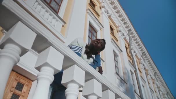 Um jovem negro posa contra o pano de fundo de um belo edifício de teatro — Vídeo de Stock