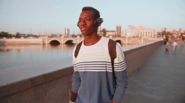 Gün batımında şehir merkezinde kulaklıklı genç bir zenci öğrenci yürüyor.