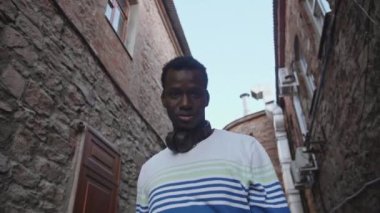 Gün batımında şehir merkezinde kulaklıklı genç bir zenci öğrenci yürüyor.