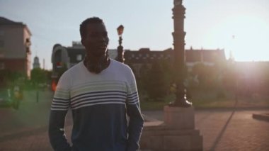 Gün batımında şehir merkezinde kulaklıklı genç bir zenci öğrenci yürüyor.