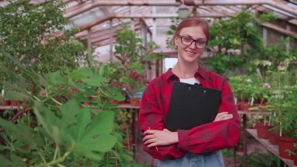 Porträt einer jungen Arbeiterin eines Gewächshauses, in dem Blumen und Pflanzen wachsen, das Mädchen Inspektorin — Stockvideo