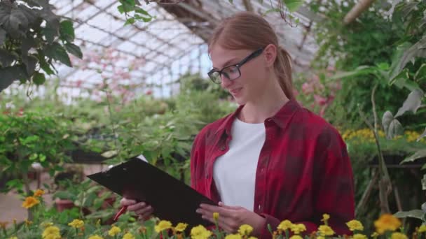 Retrato de um funcionário jovem de uma estufa na qual flores e fábricas se cultivam, o inspetor de menina — Vídeo de Stock