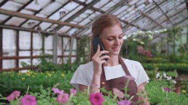 Güzel bayan çiçekçi mağaza müdürünün cep telefonuyla müşteriyle bitkiler hakkında konuşurken çekilmiş portresi. Beyaz kadın kendi çiçekçisinde çalışıyor ve akıllı telefondan konuşuyor. Perakende kavramı