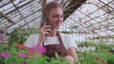 Güzel bayan çiçekçi mağaza müdürünün cep telefonuyla müşteriyle bitkiler hakkında konuşurken çekilmiş portresi. Beyaz kadın kendi çiçekçisinde çalışıyor ve akıllı telefondan konuşuyor. Perakende kavramı