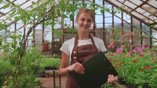 Mujer jardinero comprueba la calidad de las plantas, toma notas en la tableta digital, caminando a lo largo de centro de jardín o invernadero. cultivar y cuidar las plantas. floristería, jardinería, horticultura, floristería. — Vídeo de stock