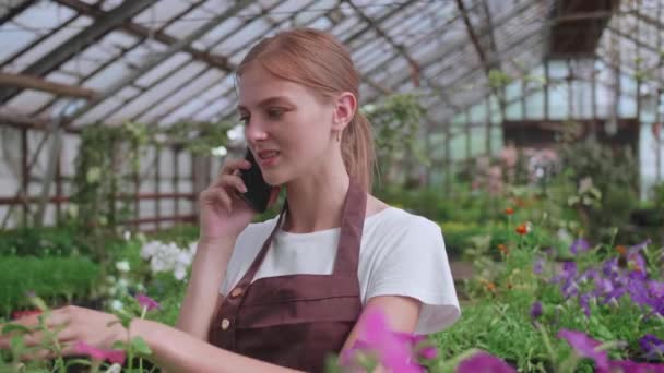 Zavřít portrét krásné radostné ženské květinářství manažer obchodu mluvit na mobilu o rostlině s klientem. Běloška pracující ve vlastním květinářství a mluvící na smartphonu. Maloobchodní koncept — Stock video