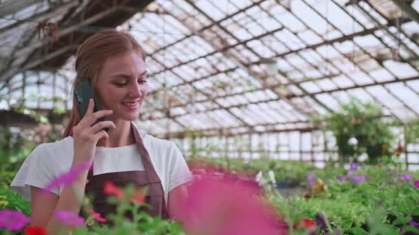 顧客と植物について携帯電話で話す美しい喜びの女性花屋の店のマネージャーの肖像画を閉じます。自分の花屋で働く白人女性やスマートフォンで話す。小売コンセプト — ストック動画
