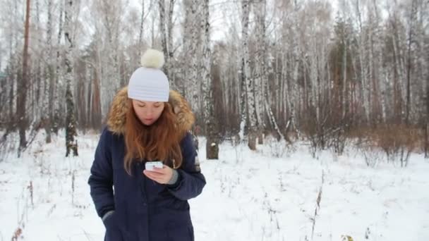 Девушка, гуляющая в зимнем лесу с телефоном — стоковое видео