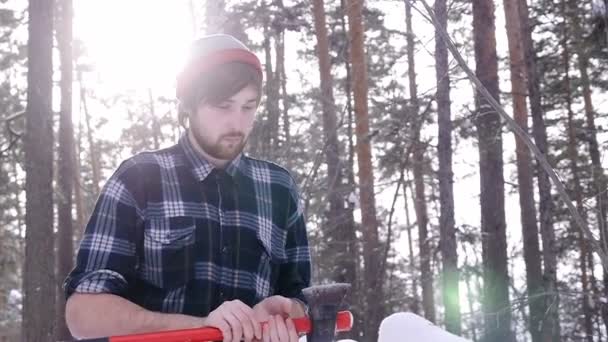 Oduncu ayağa kalkar ve ormanda baltasını keskinleştirir, ışık kaçağı onu çevreler. — Stok video