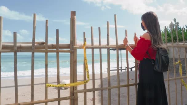 Una giovane ragazza sola con i capelli lunghi, vestita con una camicetta rossa, si trova al recinto di bambù.. — Video Stock