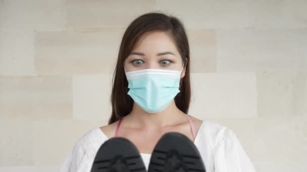 Tıbbi maskeli büyük yeşil gözlü genç bir kız, yeni siyah ayakkabılarıyla seviniyor.. — Stok video