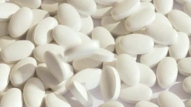Fabrikada yeni beyaz vitamin tabletleri üretiliyor. Beyaz haplar aynı ilaçlarla dönen bir platforma düşer. Tüm bunlar parlak ışık ve zıt gölgelerin içinde. yavaş çekim