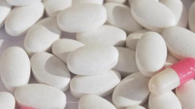 Beyaz tabletler ve parlak pembe kapsüller ışık yüzeyinde dönerler. Coronavirus aşısının yerini alacak yeni kapsüllerle bağlantılı ilaçların sergilenmesi. Yakın çekim ve üst görünüm.