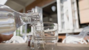 Garson masanın üzerinde duran temiz bir bardağa bir şişeden su döker. Güneşli bir günde, restoranın yaz terasında, insanlar olmadan. Tek müşterisi olan boş bir restoran. Yavaş.