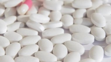 Beyaz tabletler ve parlak pembe kapsüller ışık yüzeyinde dönerler. Coronavirus aşısının yerini alacak yeni kapsüllerle bağlantılı ilaçların sergilenmesi. Yakın çekim ve üst görünüm.