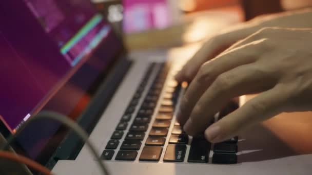 O programador de hackers começa a trabalhar. Uma pessoa estende os dedos e liga um programa de computador para escrever código, contra o fundo de monitores e uma bela luz laranja. Fechar. — Vídeo de Stock