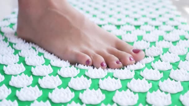 A girl with a beautiful dark red manicure stands on a Chinese green massage mat with white spikes. The girl begins to engage in body practices and meditation. Working with acupuncture of the legs. — Stock Video