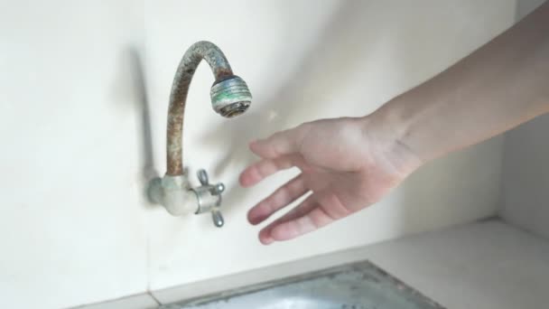 A person turning on the old iron, rusty tap on a background of white tiles. From a vintage tap with a green coating, water begins to flow into an iron sink in a white space. Slow motion. — Stock Video
