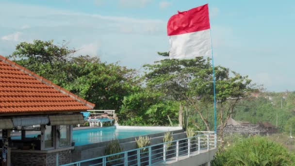 Wspaniały hotel z wielką flagą Indonezji, niebieski basen na dachu i samotnych turystów opalania. Pusty tropikalny hotel z jednym turystą ze względu na pandemię na wyspie Bali. — Wideo stockowe