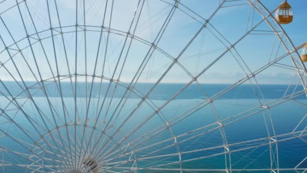 Aerial shot of a large white Ferris wheel with colored blue and yellow cabins. Behind the big wheel, idyllic landscape opens with a blue lake and against the background of white mountains of glaciers — Stock Video