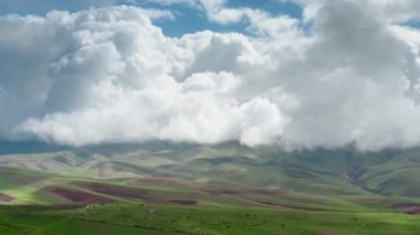 Yeşil tepeleri ve kahverengi tarlaları olan muhteşem bir hava manzarası dönen büyük beyaz bulutların altında. Fırtınalı bulutlu görkemli bir gökyüzünün altında tarımsal tarlaların destansı manzarası.