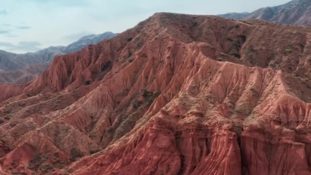 Un vol fascinant à travers le sommet d'une énorme roche rouge et la découverte d'un paysage profond avec des dunes de sable contre un ciel nuageux bleu. Rochers rouges uniques par une journée ensoleillée en été capturés sur un drone — Video