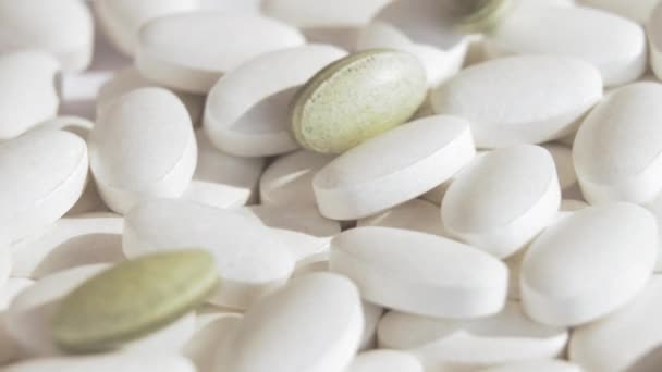 Produção farmacêutica novas pílulas verdes caem em comprimidos brancos comuns que giram em uma plataforma branca. Produção de comprimidos de cannabis, comprimidos de ervas, indústria farmacêutica. Movimento lento. Fechar. — Vídeo de Stock