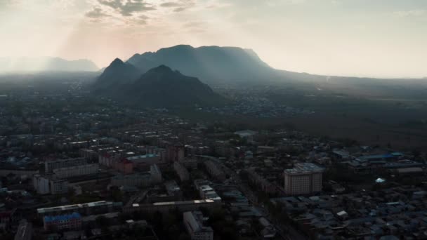 Un misterioso paisaje místico de la ciudad a la sombra al pie de una gran roca negra en los rayos de la luz del sol poniente que atraviesa las nubes. Un tiro tenso de una ciudad mágica oscura. — Vídeo de stock