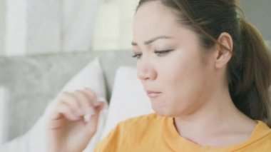 Genç, güzel, melez bir kız hasta ve yatakta oturuyor. Sarı tişörtlü üzgün bir kadın parlak bir evin içinde öksürüyor, ilaç içiyor ve su içiyor. Evde tedavi.