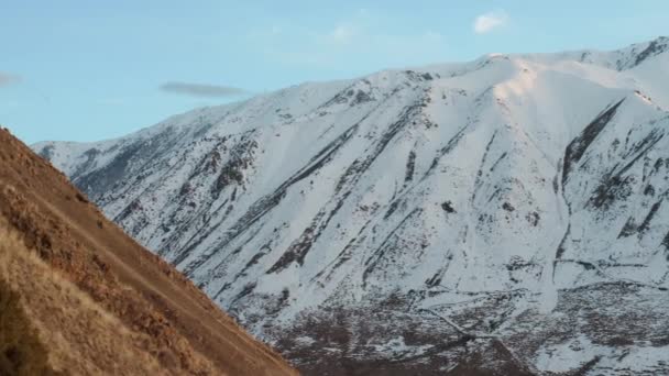 白い雪に覆われた大きな山に砂石の丘を過ぎて絵のように美しい航空便。白い雲と青い空と夕日の光の中で美しい山の風景. — ストック動画