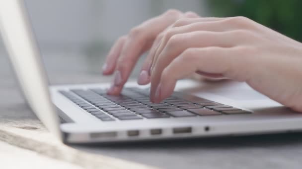 Seorang gadis pekerja lepas mengetik surat tentang pekerjaan di papan ketik laptop. Close-up of a womans fingers typing on a computer, against the background of a green garden on a sunny day. Bekerja daring. — Stok Video