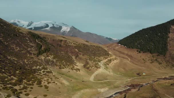 緑の山々、道路、小さな白い家がある大きな谷のある風通しの良い絵のような風景、雪の斜面がある大きな山と雲のある青い空の背景. — ストック動画