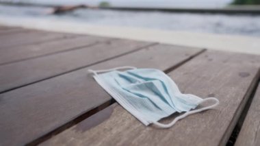 Mavi bir tıbbi maske, güneşli bir günde yüzen bir adamın mavi bir havuzun arka planında, ahşap zeminde yatar. Maske rejiminden ve virüsün tacının ardındaki kısıtlamalardan kurtulmak.