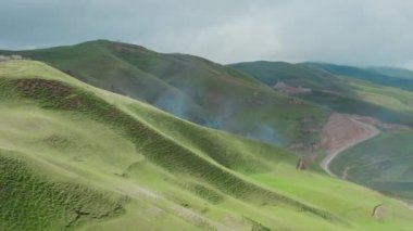 Güneş ışınlarında mavi dumanlı yeşil dağların olduğu güzel bir manzaranın havadan görünüşü. Güzel dağlarla sabah manzarası, bir yol ve tepelerden oluşan bir vadi ve bulutlu mavi gökyüzü.. 