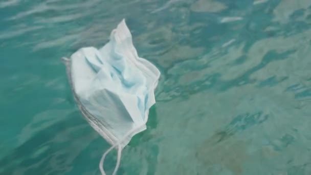 海に浮かぶ医療用マスクの上からの眺め 太陽のまぶしさと緑の水 コロナウイルスのパンデミックの結果は 使い捨てマスクのために形成された環境とゴミに関連している 高品質4K映像 — ストック動画