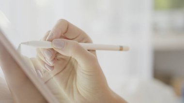 Tasarımcı bir kız tablete kalemle parlak bir iç çekimde resim çiziyor. Güzel pembe manikürlü bir kadın tablet üzerinde çalışıyor ve gelecekten bir çerçeve kullanıyor. Ağır çekim. Yüksek kalite fotoğraf