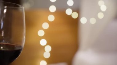 Güzel, parlak bir Noel çelengine kırmızı şarapla kadeh tokuşturan bir adamla bir kadının yakın çekimi. Birbirini seven insanlar tatili ve bardakları sıcak, hoş bir atmosferde tokuşturmayı kutlarlar.. 