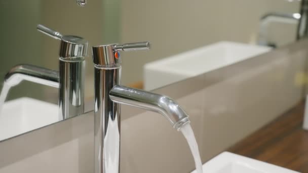 Un hombre cierra un hermoso grifo brillante sobre el fondo de un fregadero blanco y una encimera de madera. Una hermosa mano de hombre cierra el nuevo grifo de cromo, y el agua cristalina deja de fluir desde — Vídeos de Stock