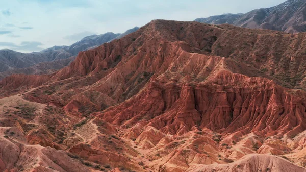 Een ongewoon luchtlandschap met enorme roodbruine rotsen en een berg waarop een man in een rood T-shirt zit te mediteren. Een verlaten ravijn met kloven gefilmd op een helikopter op een zonnige dag. — Stockfoto