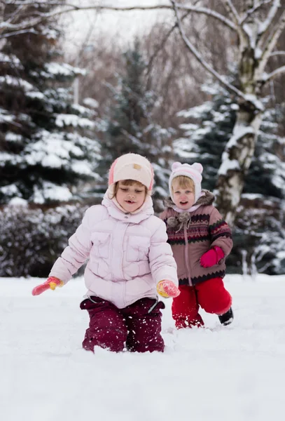 Two funny adorable little sisters building a snowman together in — Stock Photo, Image