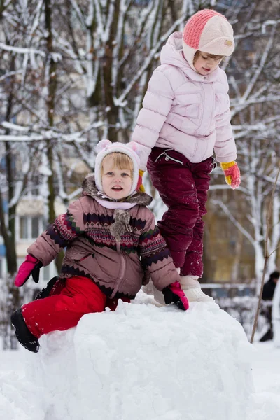 Two funny adorable little sisters building a snowman together in — Stock Photo, Image