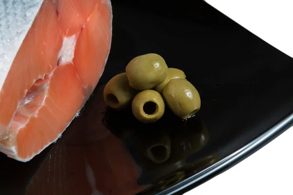 Шматок лосося на чорній тарілці з оливками — стокове фото