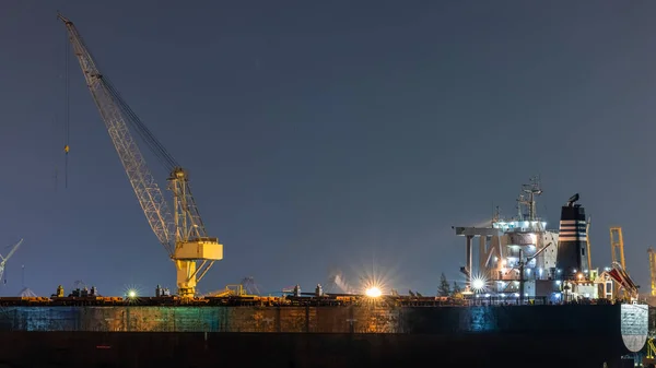 container oil tank ship repairing and maintenance on shipyard dry dock Industry at night over lighting Equipment and water front long exposure shot