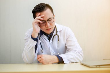 Üniformalı Asyalı genç doktor ofisindeki bir sandalyede otururken stresli oluyor. 