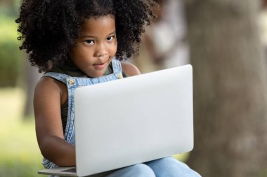 Çocuklar, Afrika kökenli siyah tenli Afro-Amerikalı kızlar ağaçta oturuyorlar. İnternette bilgisayarla oyun oynuyorlar. Parkta kablosuz internet sinyali, sosyal mesafe konsepti üzerinden. 