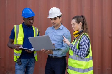 Lojistik depo ustabaşısı dizüstü bilgisayarla konuşuyor ve kadın işçiler ithalat ticaret hizmetleri kargosundaki konteynır kutularının listesini kontrol ediyor.